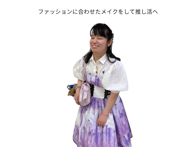 白いブラウスに紫色の花柄ワンピースを重ね、黒いウエストベルトと淡いピンクのバッグを合わせたH様。好きなファッションを身につけ、その日の服装に合わせて色を選んだメイクをして笑顔で立っている。ブラインドメイクレッスン後、自分でメイクをすることを楽しんでいる様子。